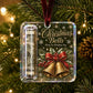A Christmas ornament hanging on a tree branch, featuring a clear square case with a rolled dollar bill bell and gold bells printed on the front, with the text 'Christmas Bells Ring In Holiday Joy' and a red ribbon bow with red berries. The background shows blurred Christmas lights and pine needles.