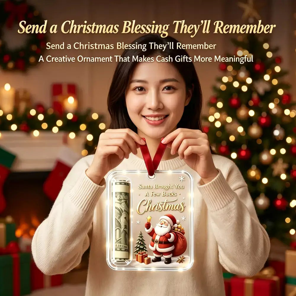 A woman in a cream sweater holds up a personalized Christmas ornament featuring a cartoon Santa, a rolled dollar bill, and the text 'Santa Brought You A Few Books - Christmas'. The background shows a cozy, blurred Christmas tree and fireplace with warm lights.