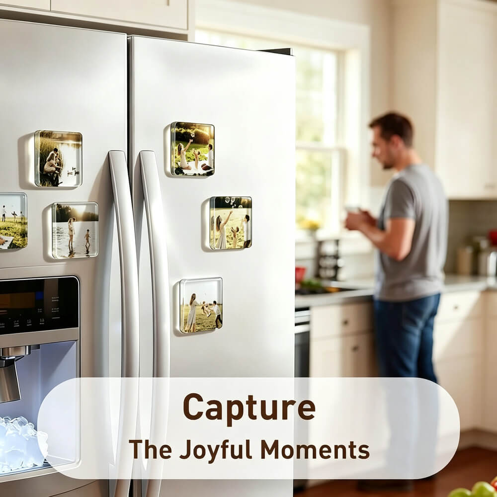 A white stainless steel refrigerator in a kitchen setting, decorated with several square clear magnets holding printed photos. A blurred man stands in the background near a window.