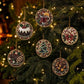 Six round beaded Christmas ornaments with holiday motifs like a cake, mug, candy canes, tree, and pinecones hanging on a decorated Christmas tree with warm lights.