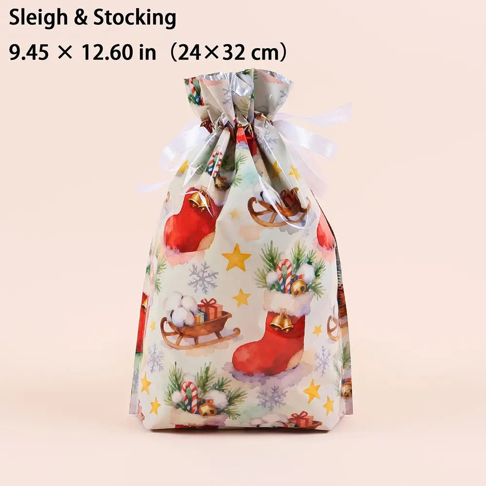 A Christmas-themed drawstring gift bag with a festive print of red stockings, sledding, candy canes, pine branches, and snowflakes on a light background. The bag is tied with a white ribbon and has text at the top reading 'Sleigh & Stocking