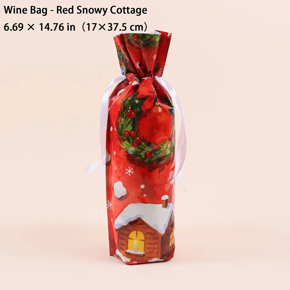 A festive red wine bag with a printed 'Red Snowy Cottage' design, featuring a green wreath, snowflakes, and a small snowy cabin. The bag is tied with a white ribbon and is shown against a solid pale pink background with a text overlay at the top detailing its dimensions.