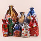 A set of Christmas-themed clear plastic drawstring gift bags with white ribbons, shown in multiple festive colors and patterns including Santa, snowflakes, holiday houses, and wreaths, arranged on a solid light beige background.