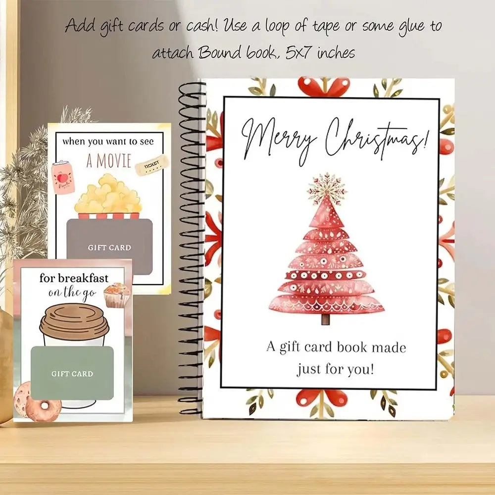 A spiral-bound Christmas gift book displayed on a wooden surface with two matching gift cards beside it. The main book cover reads “Merry Christmas!” and shows a pink watercolor Christmas tree with decorative floral border details.