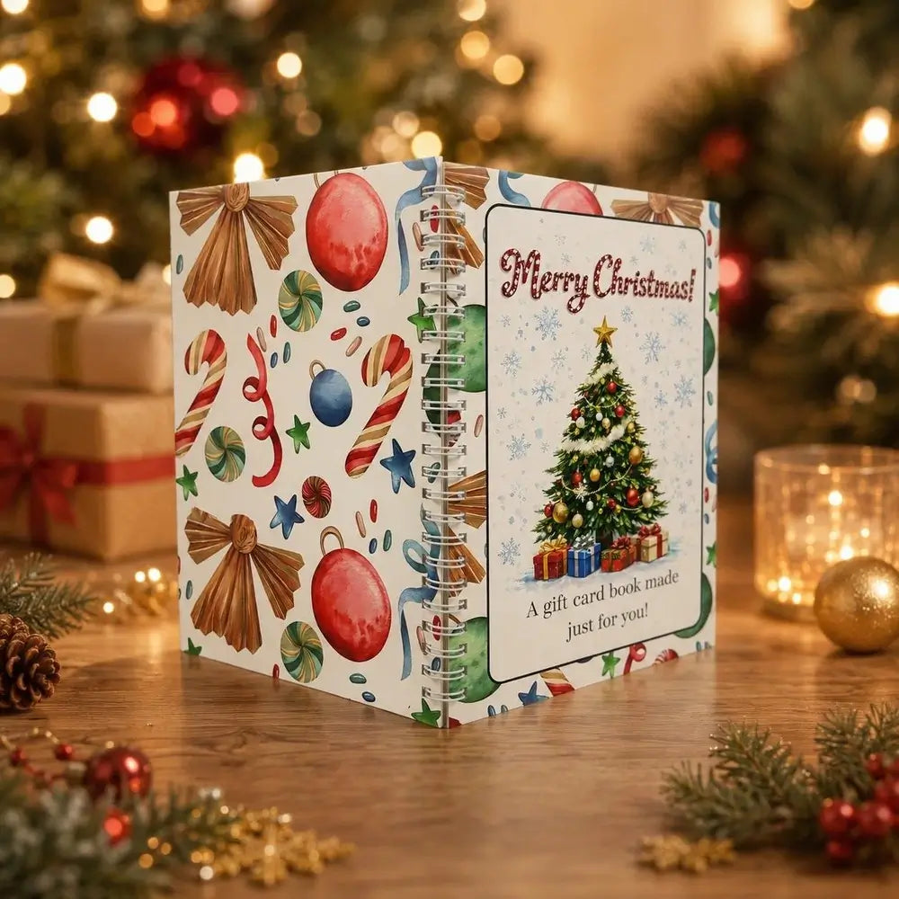 A spiral-bound Christmas gift card book standing on a wooden table, decorated with festive illustrations including a Christmas tree, ornaments, candy canes, and bows. The front cover reads 'Merry Christmas! A gift card book made just for you!' with a photo of a decorated Christmas tree.