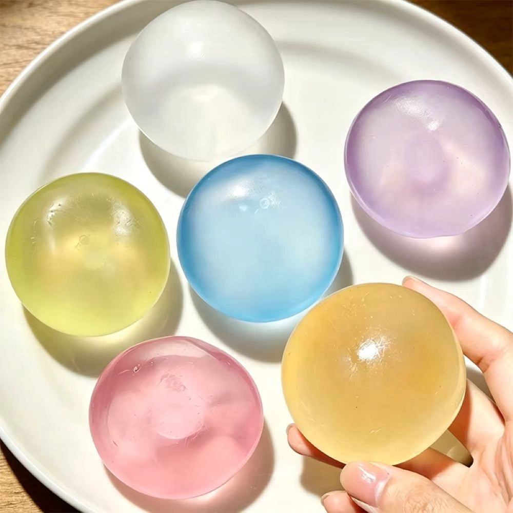 Six translucent coconut oil ball in pastel colors are arranged on a white plate, with a hand holding one amber-colored sphere in the foreground.