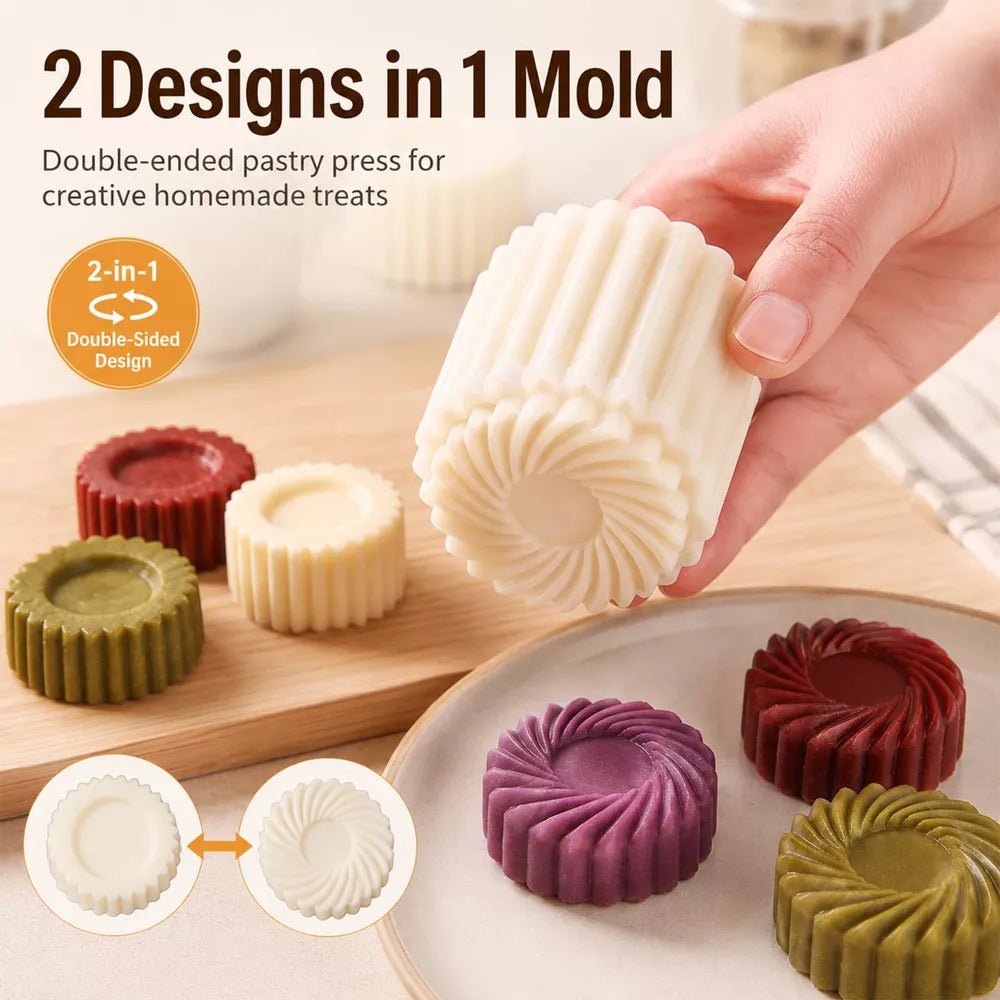 A hand holds a cream-colored pastry press mold over a plate of colorful round pastries. The image includes text reading '2 Designs in 1 Mold' and shows additional pastries in red, green, cream, purple, and burgundy, along with inset diagrams explaining the double-sided design.