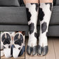Black and white spotted cow hoof socks worn on legs before a gray sofa with a sole closeup