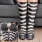Black and white striped zebra leg socks with black hoof toes worn on legs before a gray sofa