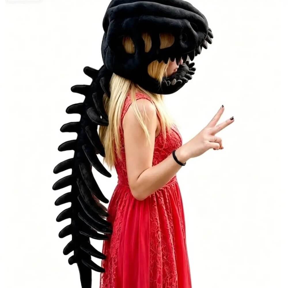 A woman in a red dress wearing a black dinosaur skull headpiece and matching black dinosaur tail costume accessory, posed against a plain white background.