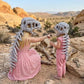A woman and a child wearing dinosaur skeleton costumes in a desert canyon setting. The woman is kneeling and pointing, while the child stands beside her.