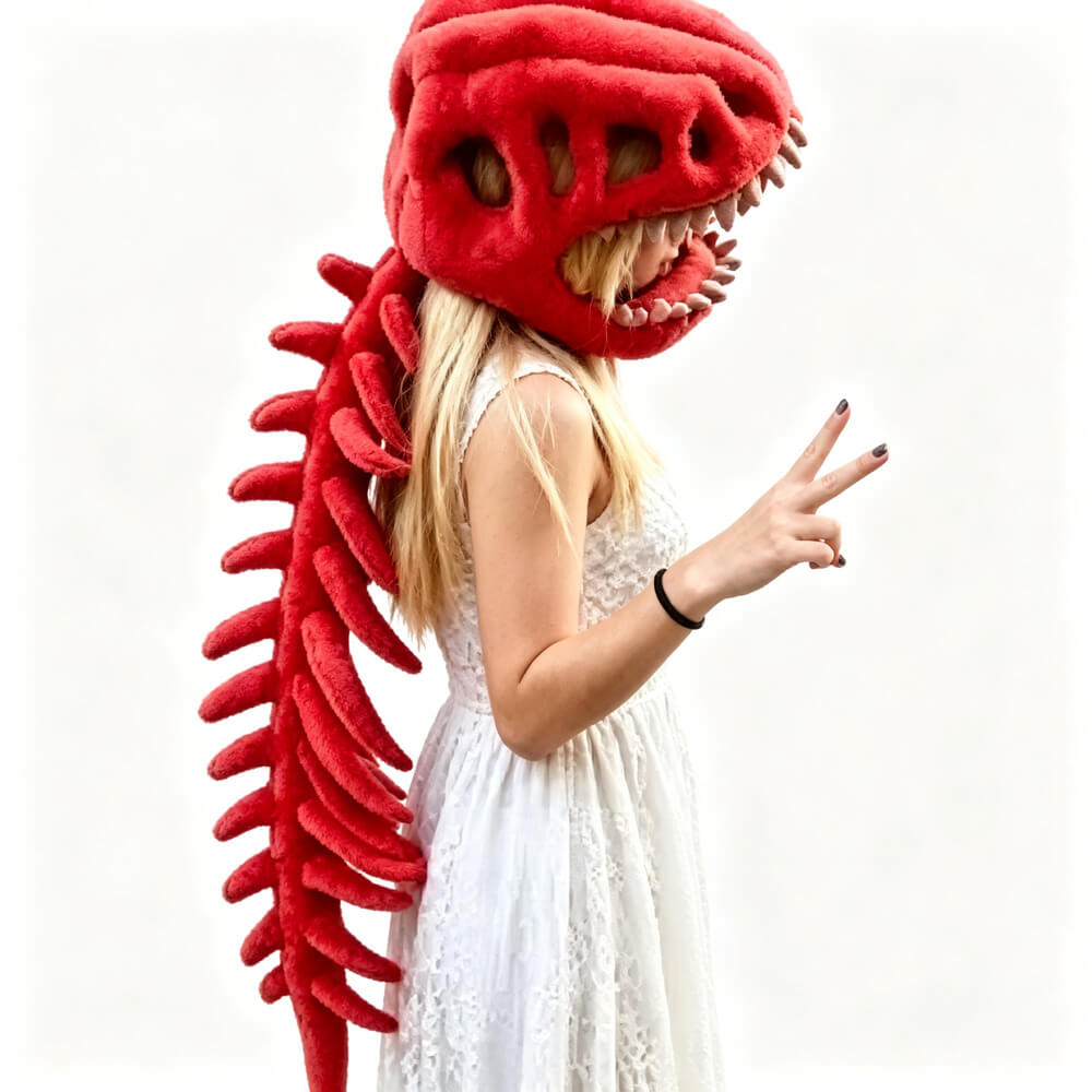 A person wearing a plush red dinosaur costume head with sharp teeth and a long red spine, posed against a plain white background while wearing a white sleeveless dress.