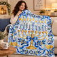 A woman wraps herself in the Hanukkah patterned blanket on a beige sofa with a lit menorah and a Happy Hanukkah mug nearby