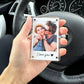 A hand holds a clear acrylic Polaroid-style photo frame in front of a car dashboard and steering wheel. The printed photo shows a couple hugging, with the text 'I love you' and a heart at the bottom.