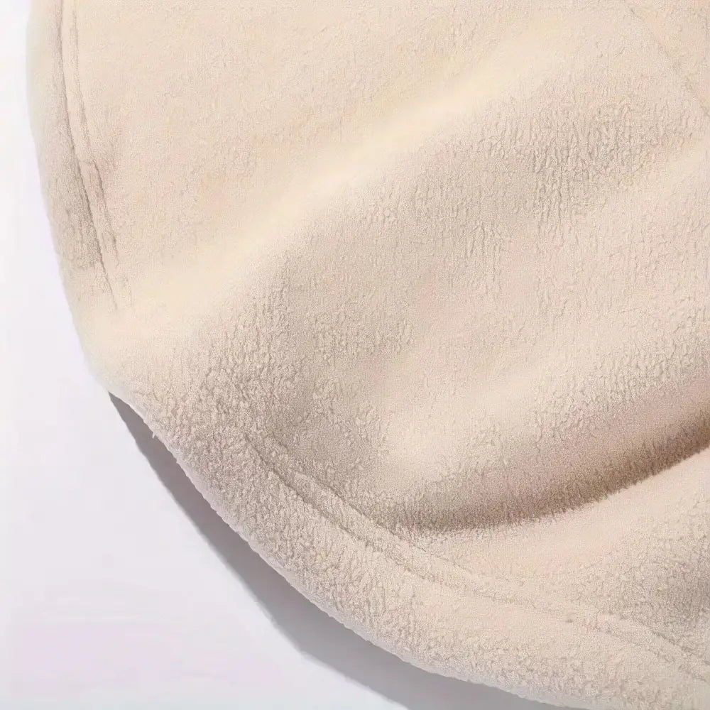 A close-up of a soft, plush fleece fabric in a warm cream or light beige color, showing its textured surface and stitched edge against a plain white background.