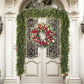 A festive Christmas wreath with red ribbons, ornaments, pinecones, and green foliage hangs on a double front door, framed by a matching green garland draped over an arched doorway.