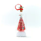 A miniature pink Christmas tree ornament inside a clear glass bottle with a cork stopper, red hanging ribbon, and white glittery base, shown on a white background.