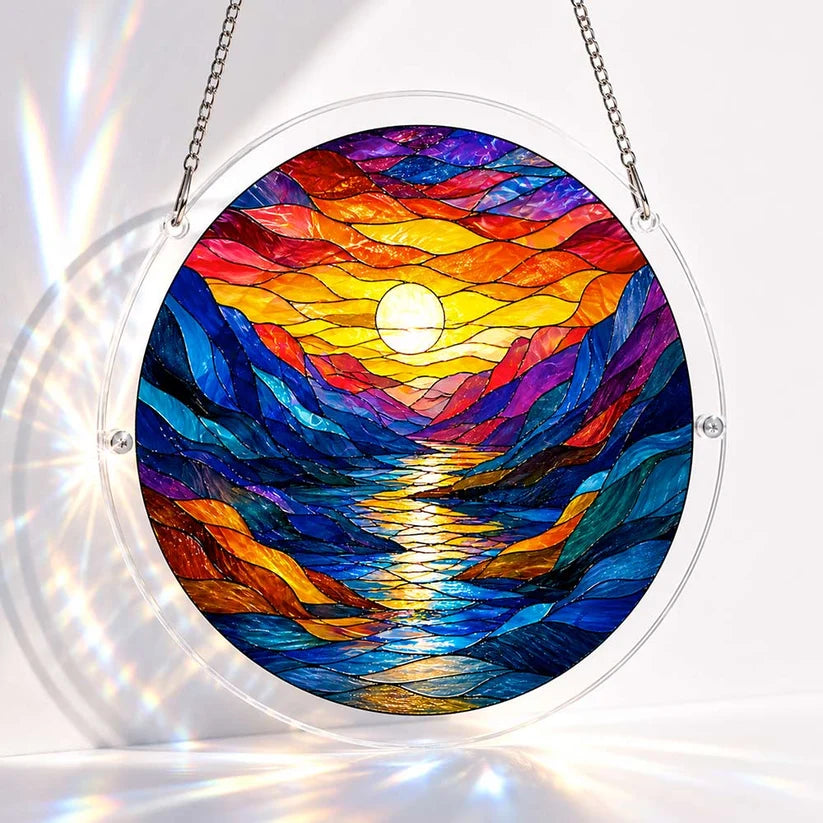 A round acrylic suncatcher of a colorful stained glass mountain river valley at sunset with the sun reflected on water