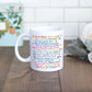 A white ceramic mug with colorful positive self-care quotes printed on it.