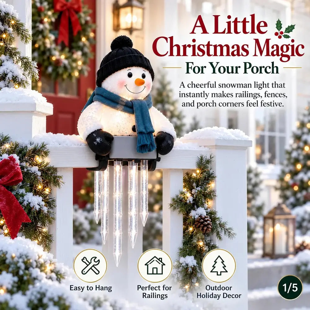 A festive snowman porch light hanging from a white fence in a decorated holiday outdoor setting. The snowman has a black hat, blue scarf, and orange nose, with clear icicle-shaped lights hanging below.