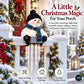 A festive snowman porch light hanging from a white fence in a decorated holiday outdoor setting. The snowman has a black hat, blue scarf, and orange nose, with clear icicle-shaped lights hanging below.