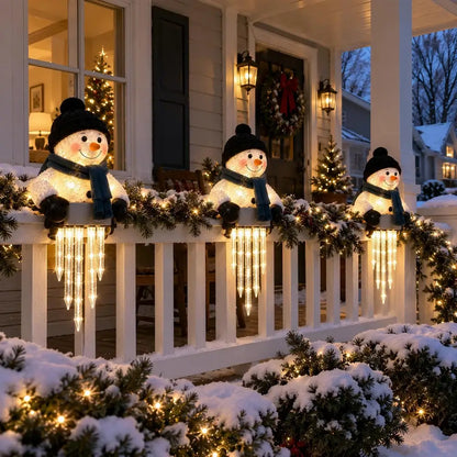 Three snowman holiday light decorations with warm white string lights are displayed on a snowy front porch with garlands and Christmas trees.