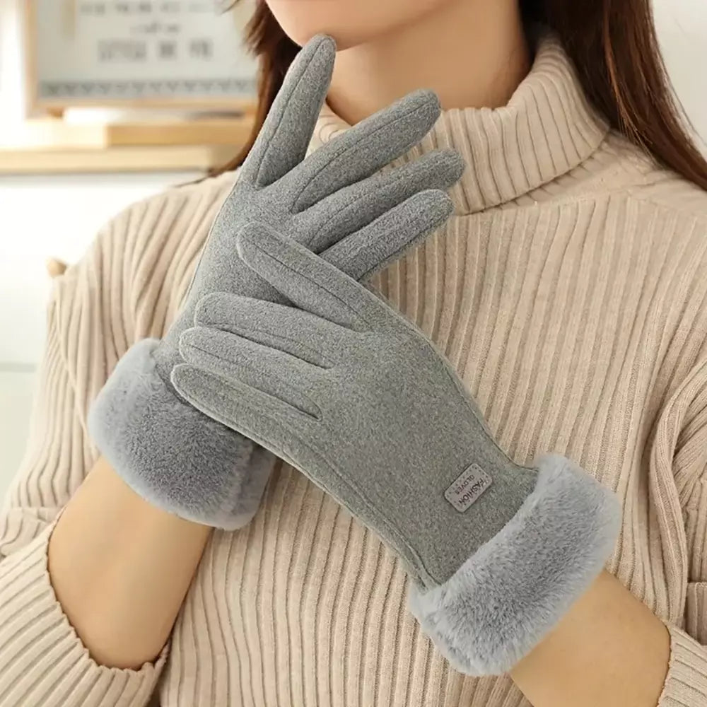 A person wearing a pair of gray fleece winter gloves with soft fuzzy cuffs, holding one glove in front of the other.