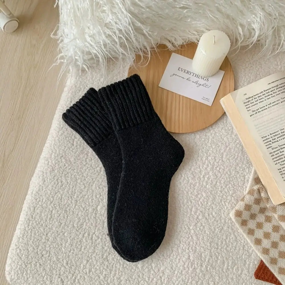 Black socks on a textured surface with a candle and book in the background