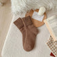Brown socks on a textured surface with a candle, card, and book in the background.
