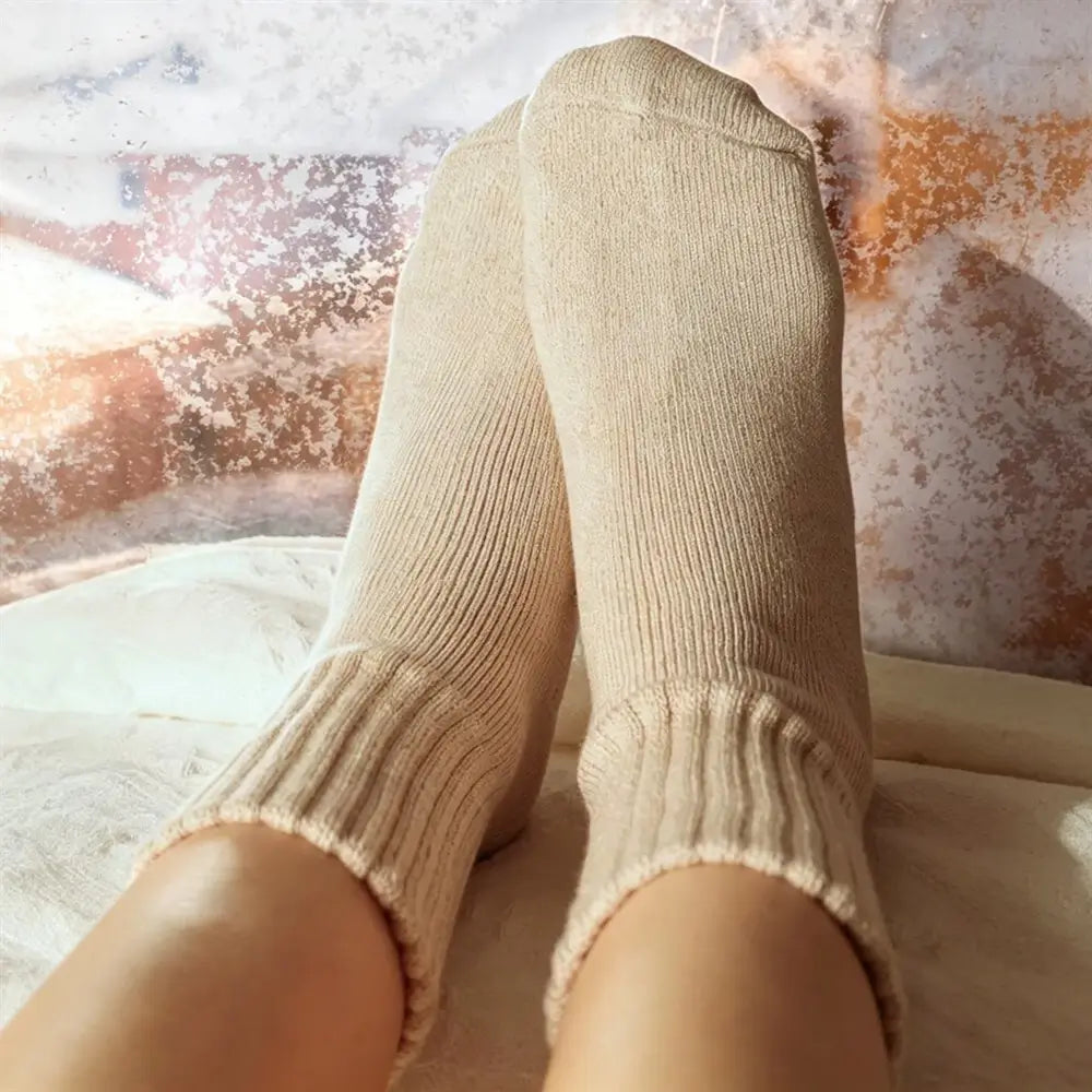A close-up of a person's legs wearing ribbed ankle socks in a warm cream or light beige color, resting against a textured, abstract background.
