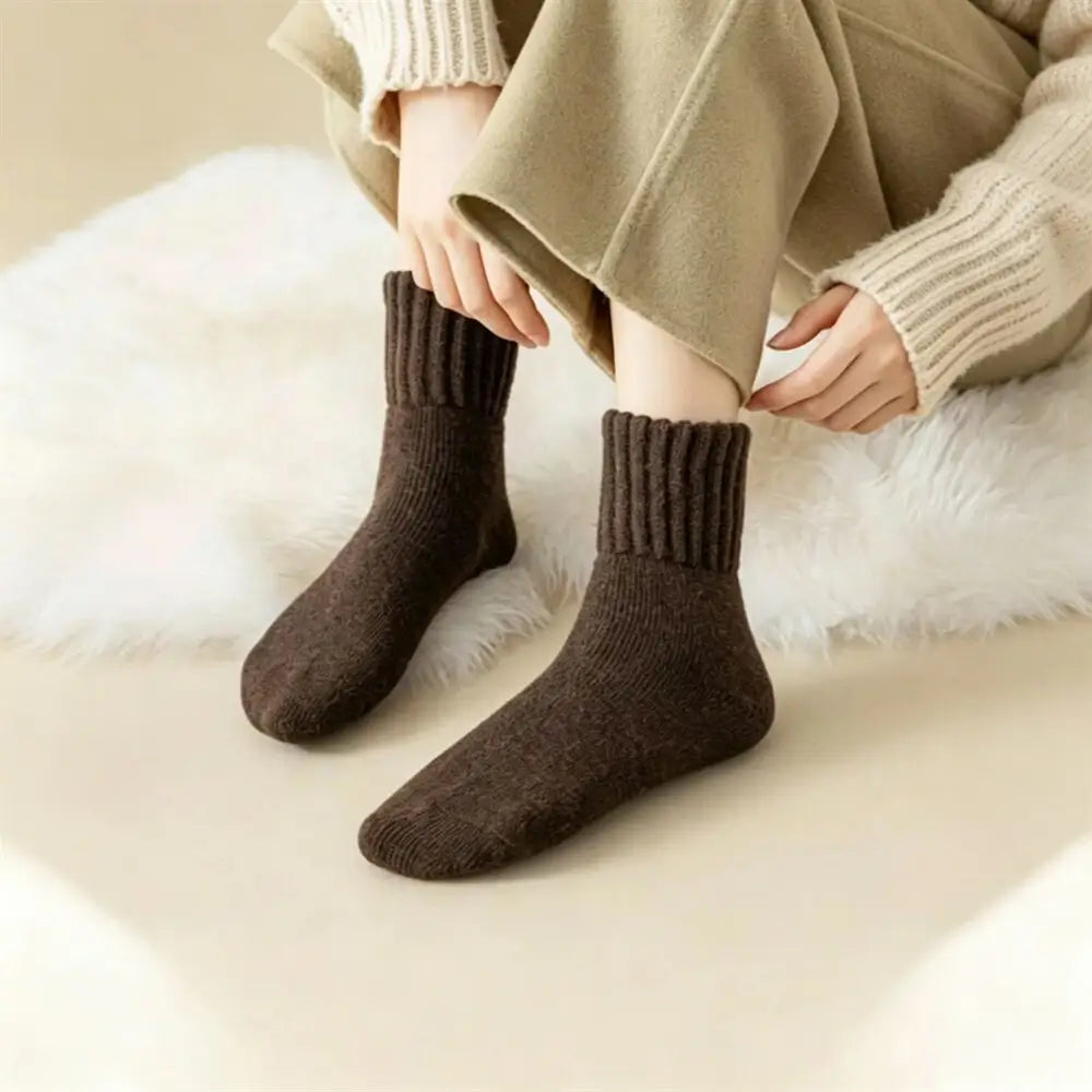 A person wearing dark brown ribbed ankle socks with a beige sweater and wide-leg beige trousers, sitting on a white faux fur rug.